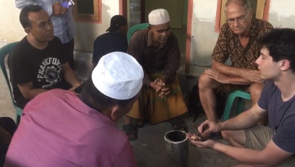 Freeze frame from the Lombok field video: the researcher sitting on the pavement with the village chief and members of the farmers' association discussing the biochar kiln.