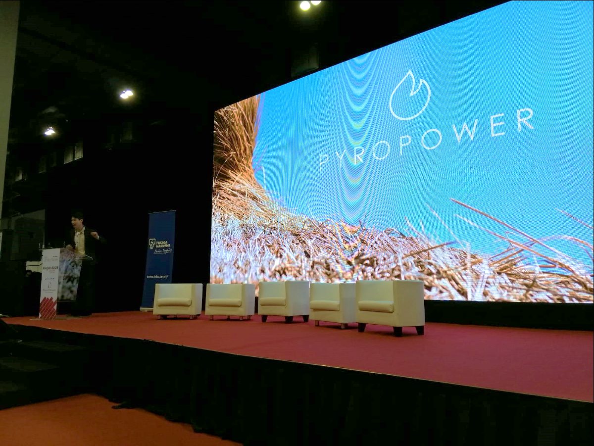 Marcel Kempers at a podium on a large stage in Kuala Lumpur, with a Pyropower slide projected on the LED wall behind him and a Tenaga Nasional banner alongside.
