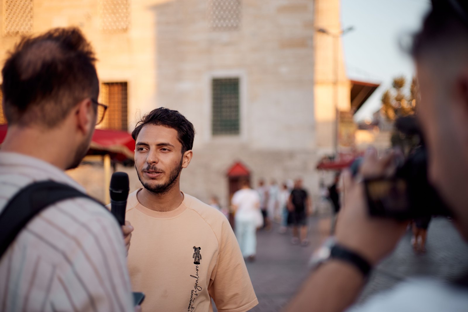A person being interviewed on a public street; another operates a camera in the foreground. Findings reaching an audience, not sitting in a final report.